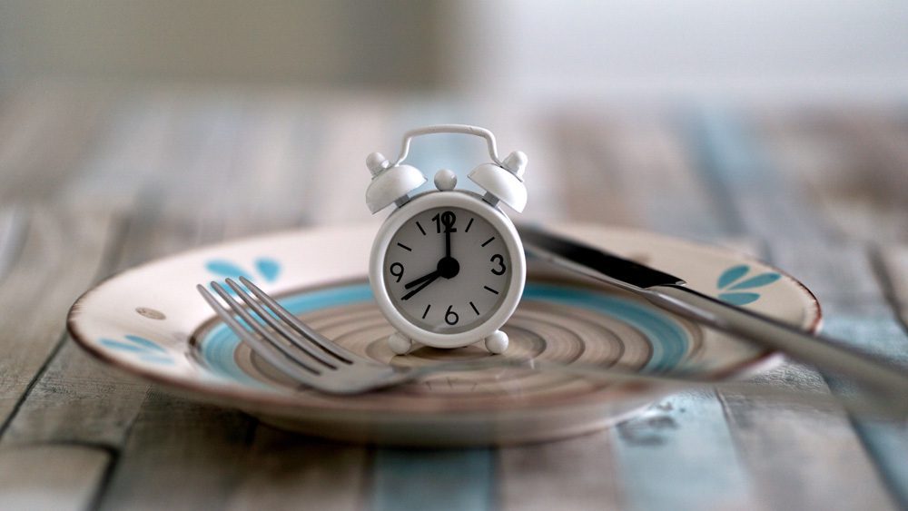 Close up view of alarm clock on a plate intermittent fasting diet Close up view of alarm clock on a plate intermittent fasting diet
