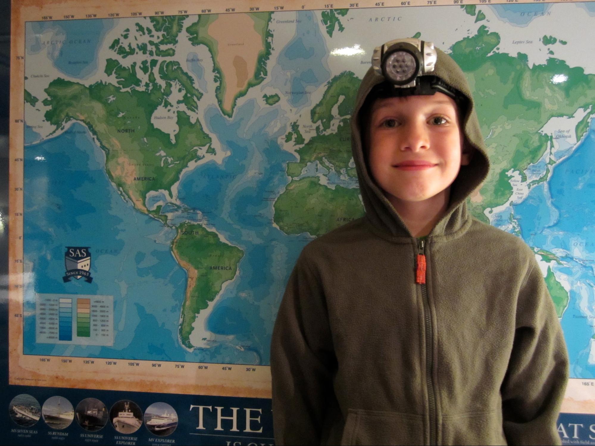 school kid smiling in front of world map