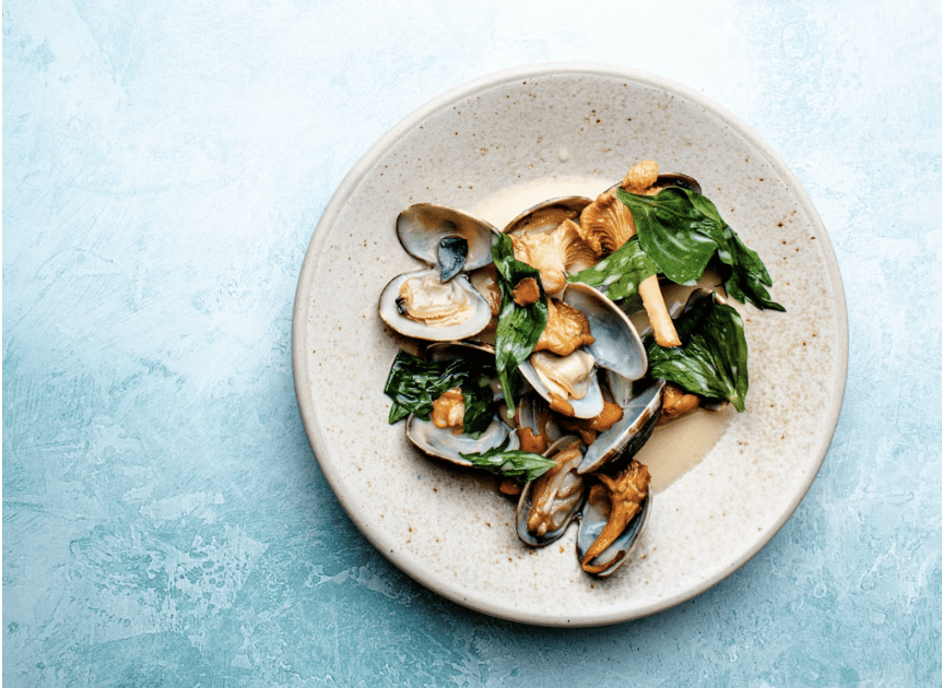 shellfish and greens plated on blue background